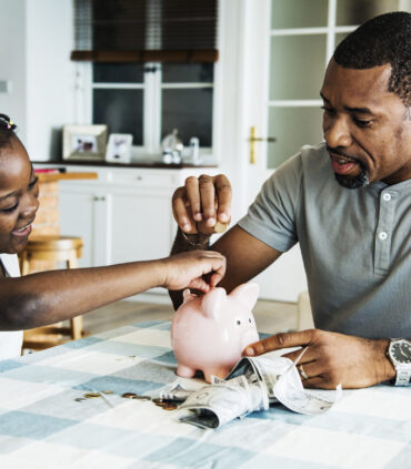 Dad and daughter saving money to piggy bank