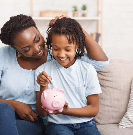 African Mother And Daughter Putting Coins Into Piggy Bank At Home. Free space