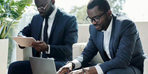 Young broker in elegant suit pressing keys of laptop keypad during network Young broker in elegant suit pressing keys of laptop keypad during network or while analyzing online financial data against colleague