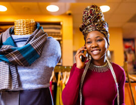 tanzanian woman with snake print turban over hear working in fabrics shop calling to client by smartphone .
